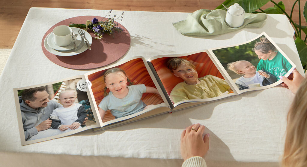 Persona mirando un fotolibro abierto en una mesa con flores y una taza.