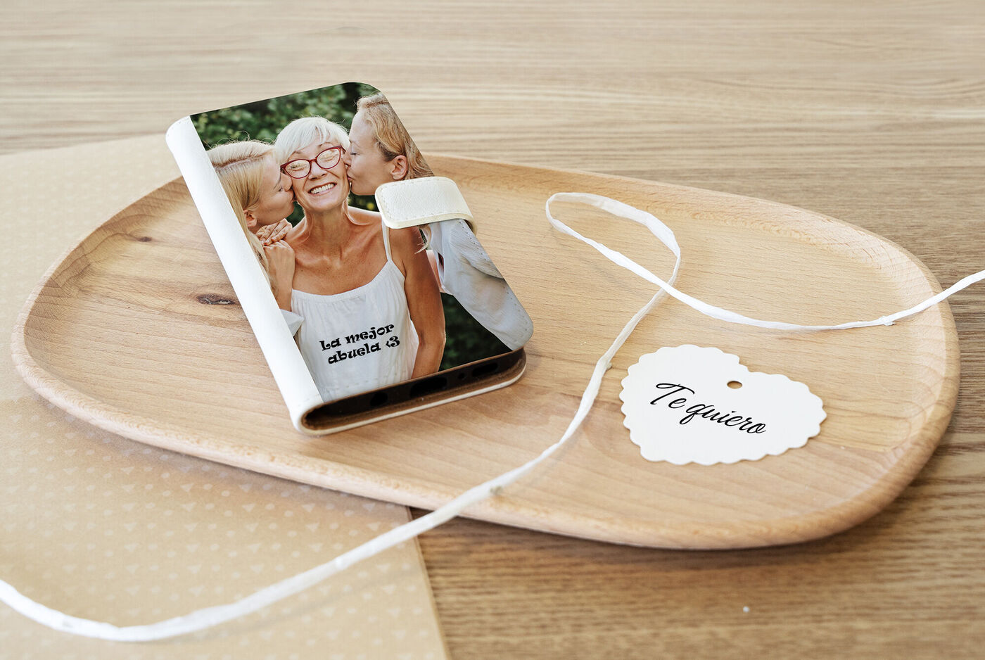 Un álbum de fotos personalizado sobre una bandeja de madera, rodeado de un mensaje cariñoso y un lazo decorativo.