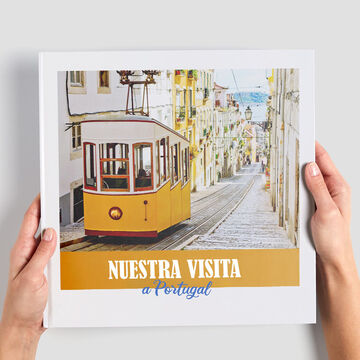 Un tranvía amarillo pasa por una calle pintoresca en Portugal. La imagen muestra a una persona sosteniendo el álbum CEWE.