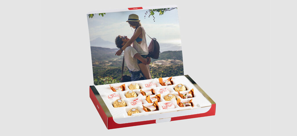 Una caja de regalo bellamente diseñada con chocolates. En la tapa hay una imagen romántica de una pareja en la playa.