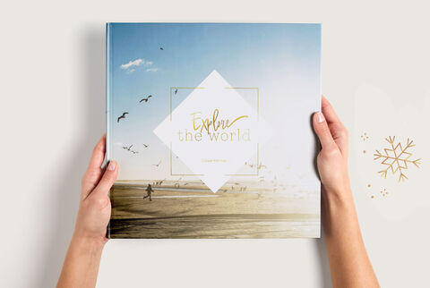 Manos sostienen un álbum CEWE con un paisaje del cielo y el mar.