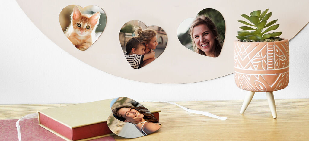 Fotos en forma de corazón cuelgan de una pared, al lado un libro de fotos y una planta moderna.