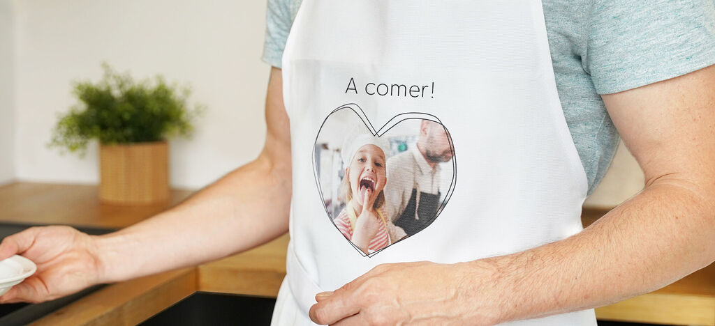 Un hombre lleva un delantal con un motivo de corazón. Contiene una imagen de un niño en un entorno acogedor.