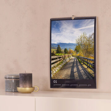 Un calendario CEWE cuelga de la pared y muestra un paisaje pintoresco con árboles y montañas.