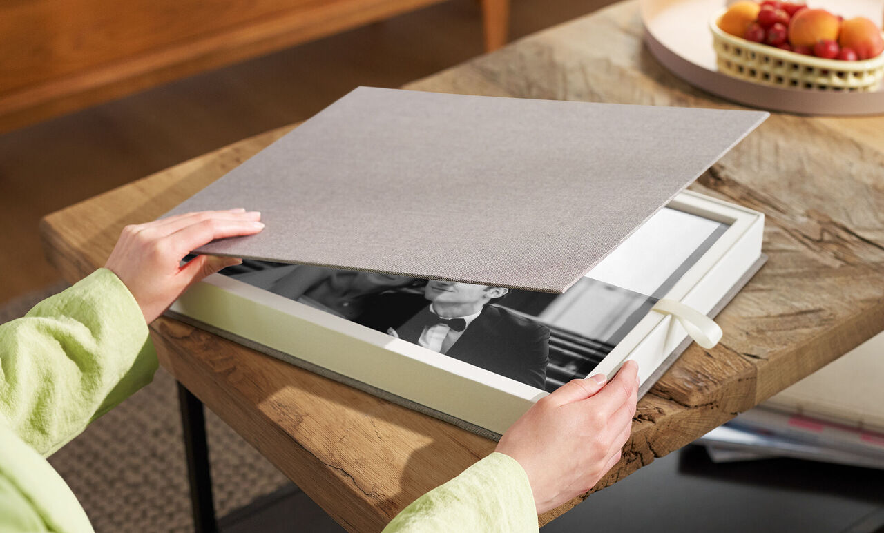 Una persona abre un libro de fotos CEWE sobre una mesa de madera.