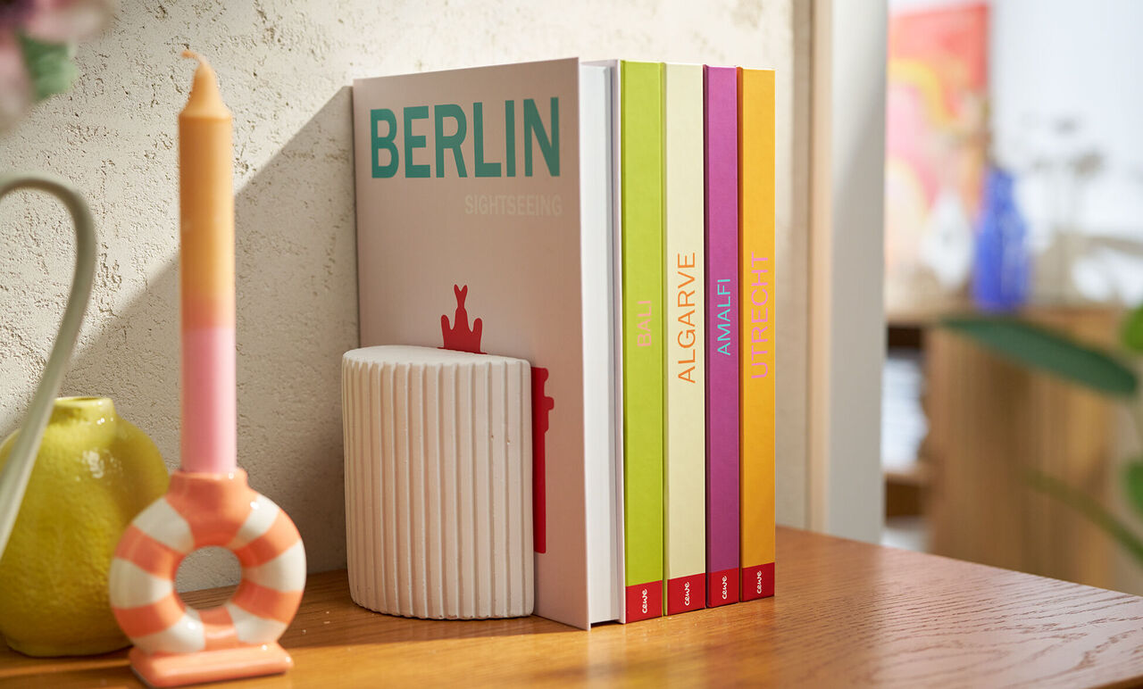 Varios álbumes de fotos de la Colección Mundo con lomos de colores, uno titulado “Berlin”, colocados en una estantería junto a objetos.