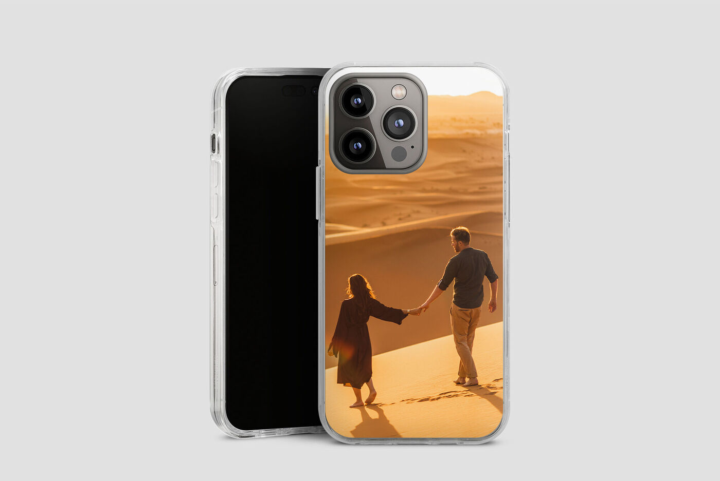 Una pareja se toma de las manos y camina por un paisaje arenoso al atardecer, sus siluetas son visibles.