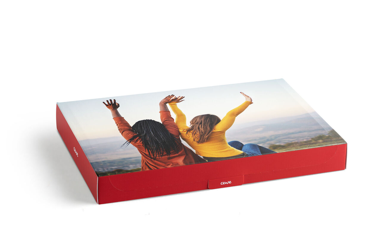 Dos mujeres sentadas en una colina saludando alegremente con su CEWE FOTOBUCH.