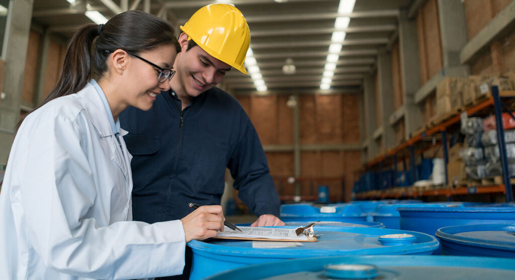Dos trabajadores discuten información importante sobre recipientes azules en un almacén.