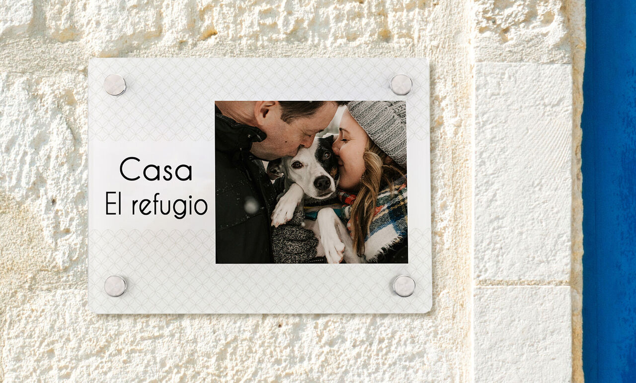 Una pareja cariñosa abraza a su perro frente a la pared de una casa.