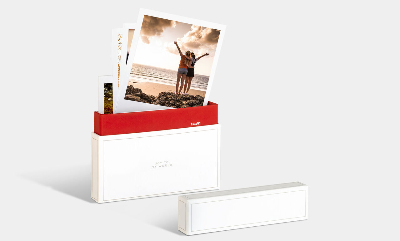 Una caja de fotos CEWE con imágenes de dos personas felices en la playa.