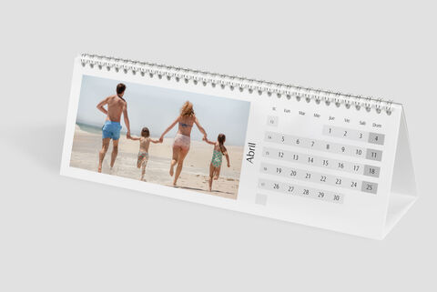 Una familia con dos niños camina de la mano por la playa sosteniendo un calendario CEWE