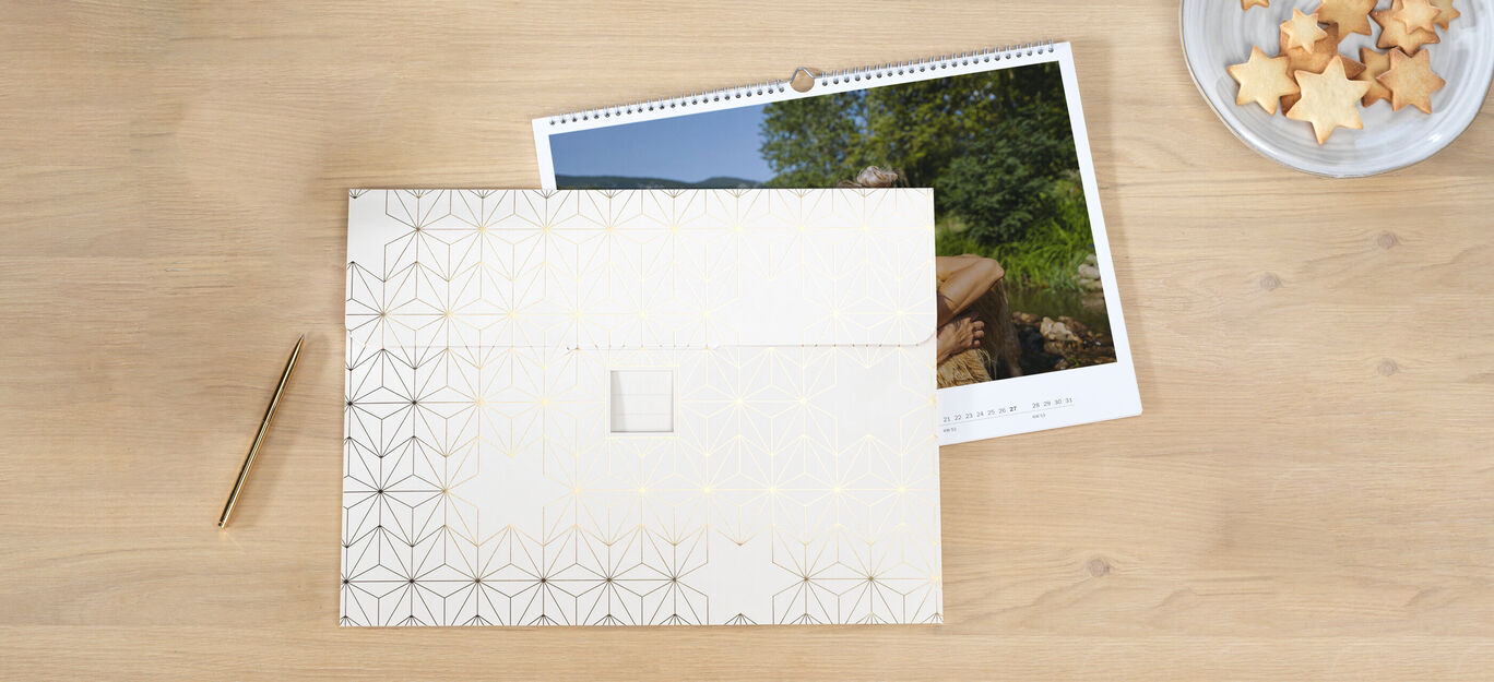 Un hermoso calendario CEWE en una mesa, junto a un plato de galletas estrella.