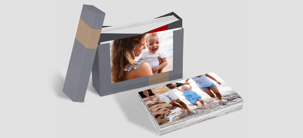 Un CEWE ÁLBUM bellamente diseñado está sobre la mesa. Muestra momentos felices de vacaciones. En la portada hay una madre y su bebé en el agua.