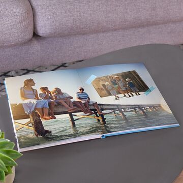 Fotobuch abierto en una mesa con recuerdos de vacaciones, familia feliz junto al agua