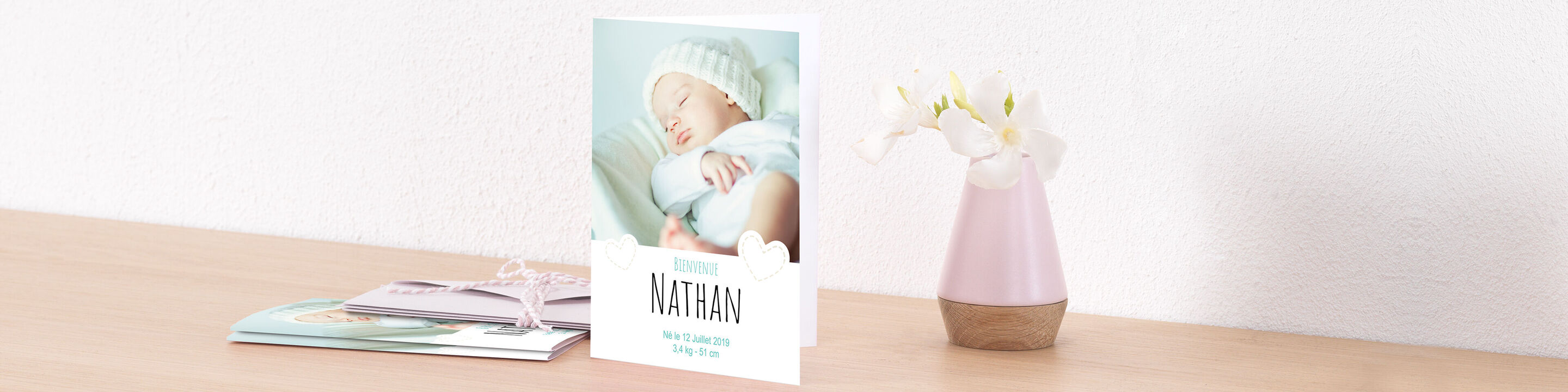 Tarjeta de saludo con el nombre Nathan y un bebé dormido, rodeado de hermosas flores en una mesa.