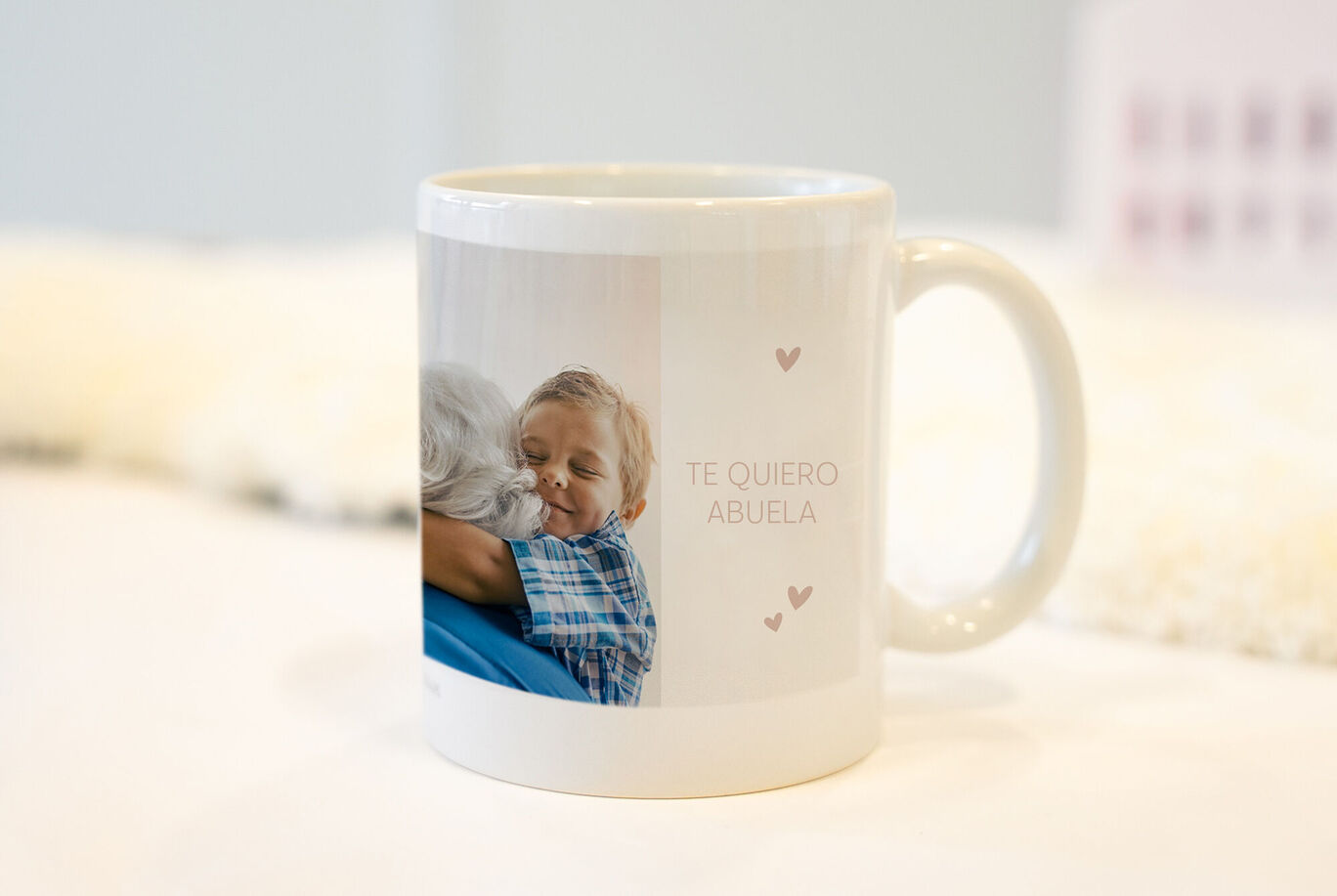 Una taza diseñada con cariño muestra un abrazo entre un niño y su abuela. Texto "Te quiero abuela" impreso.