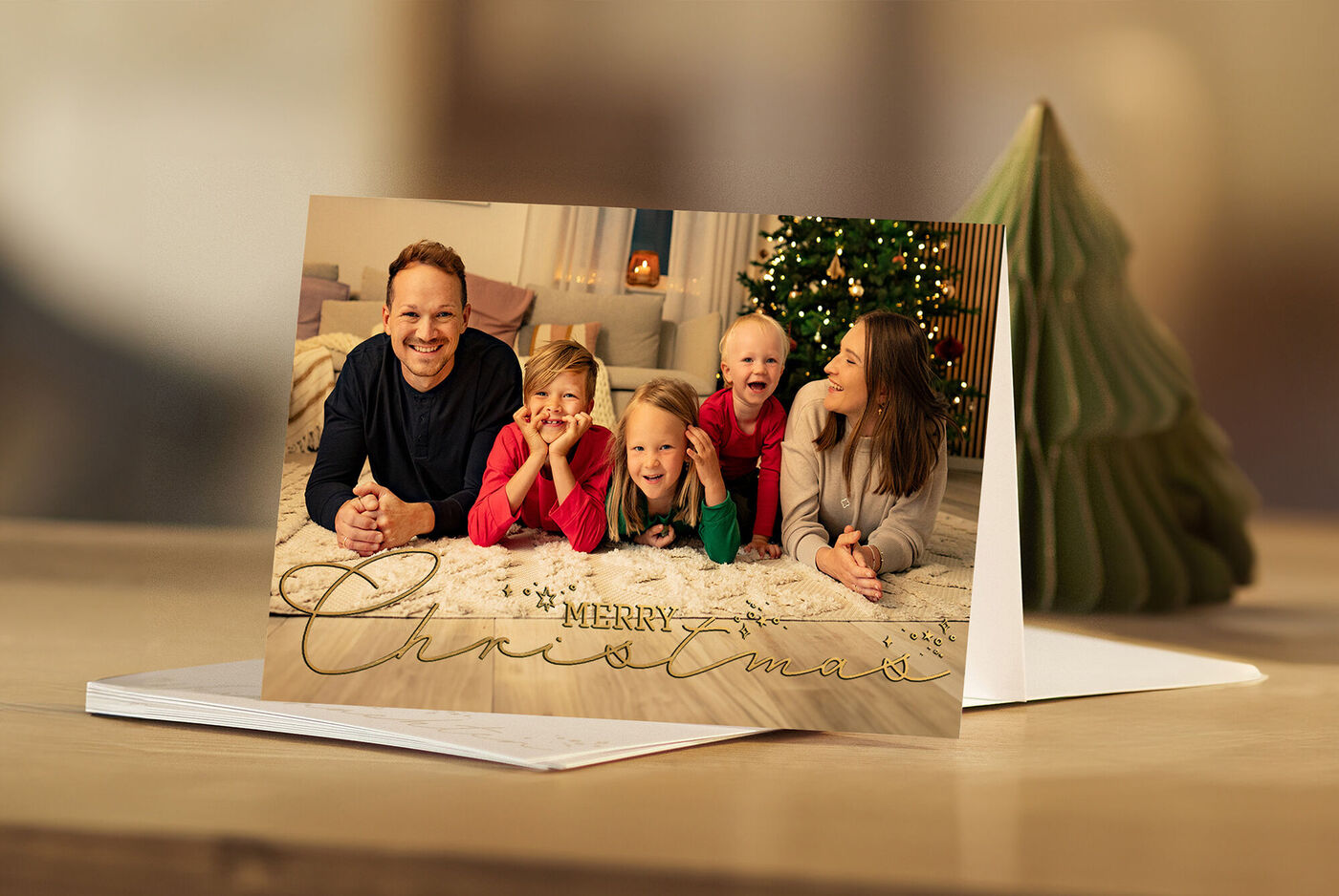 Tarjeta de felicitación navideña personalizada con foto familiar junto a un árbol de Navidad decorativo.