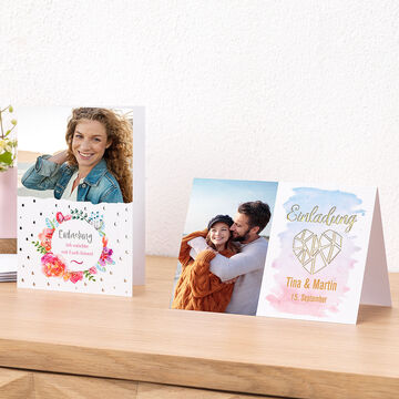 Dos invitaciones bellamente diseñadas sobre una mesa de madera, una con flores coloridas y otra en tonos suaves.