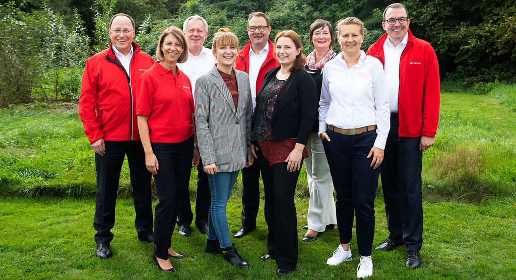 Un grupo de personas sonríe en la naturaleza. Llevan camisetas rojas y representan espíritu de equipo.