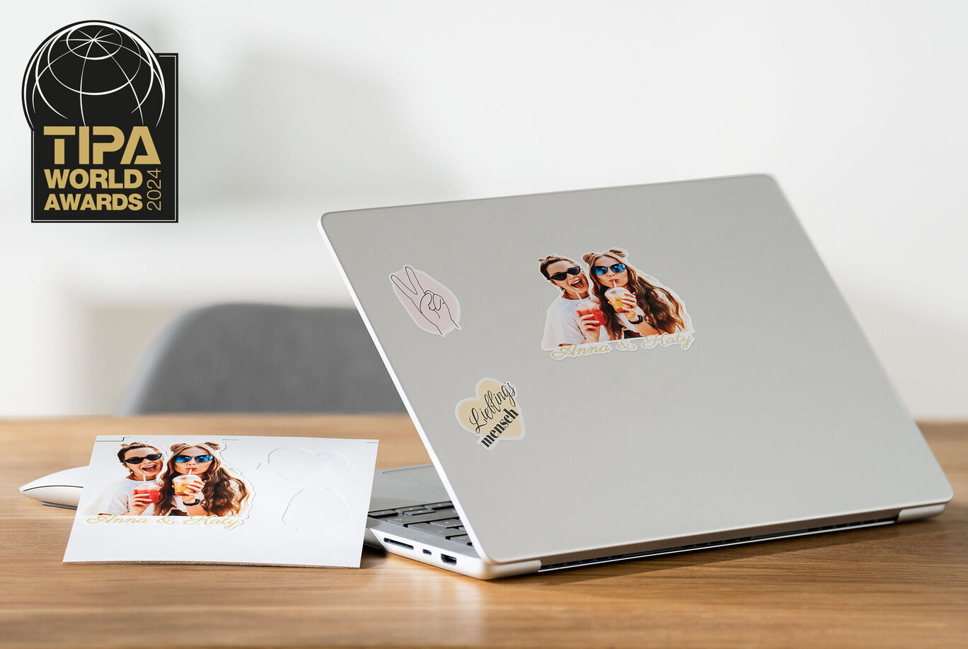 Laptop con etiquetas y una postal sobre una mesa.