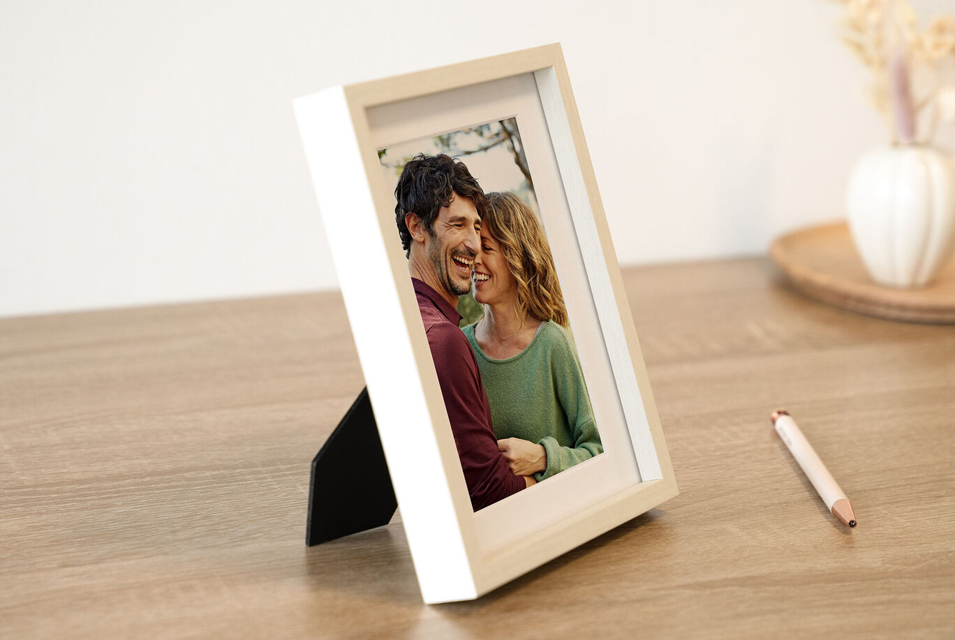 Una bonita imagen en un marco blanco sobre una mesa de madera. La imagen muestra a una pareja abrazándose cariñosamente.