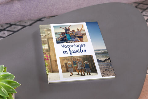 Un ÁLBUM CEWE titulado "Vacaciones en familia" sobre una mesa, con miembros felices de la familia en la playa en la portada.