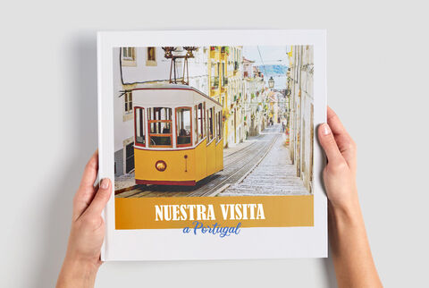 Una persona sostiene un CEWE fotolibro titulado 'Nuestra Visita a Portugal' frente a una colorida vista de la calle.