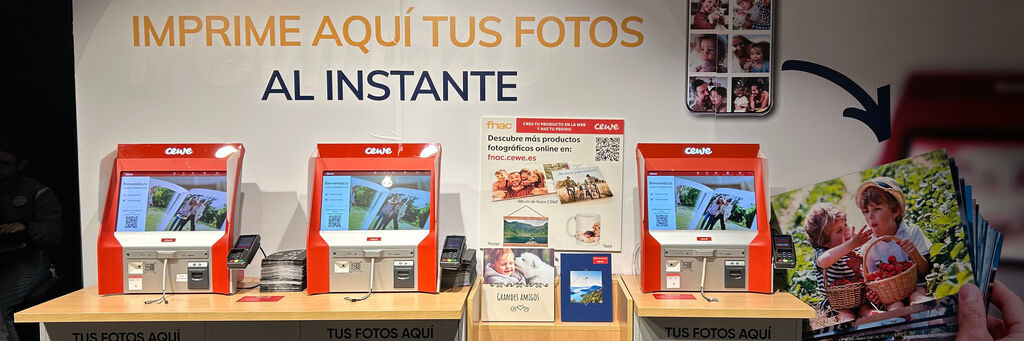 Zona de autoservicio con tres terminales de impresión de fotos CEWE, cartel promocional y decoración con imágenes de productos fotográficos.
