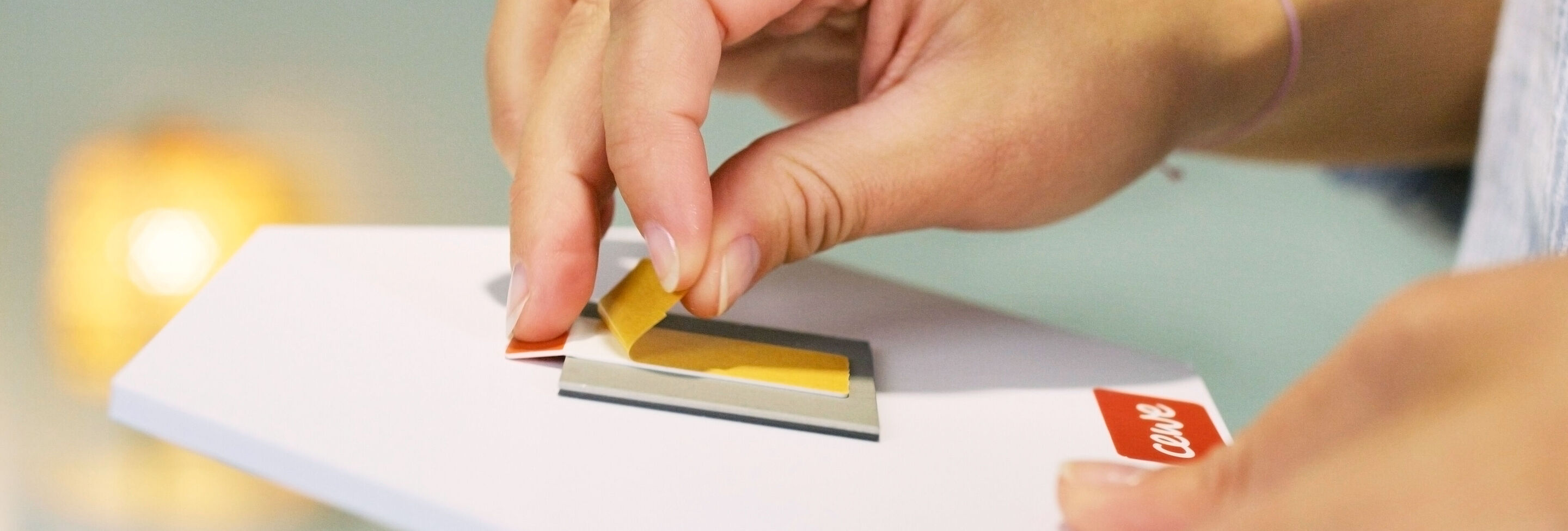 Una mano despega una lámina amarilla de una tarjeta CEWE
