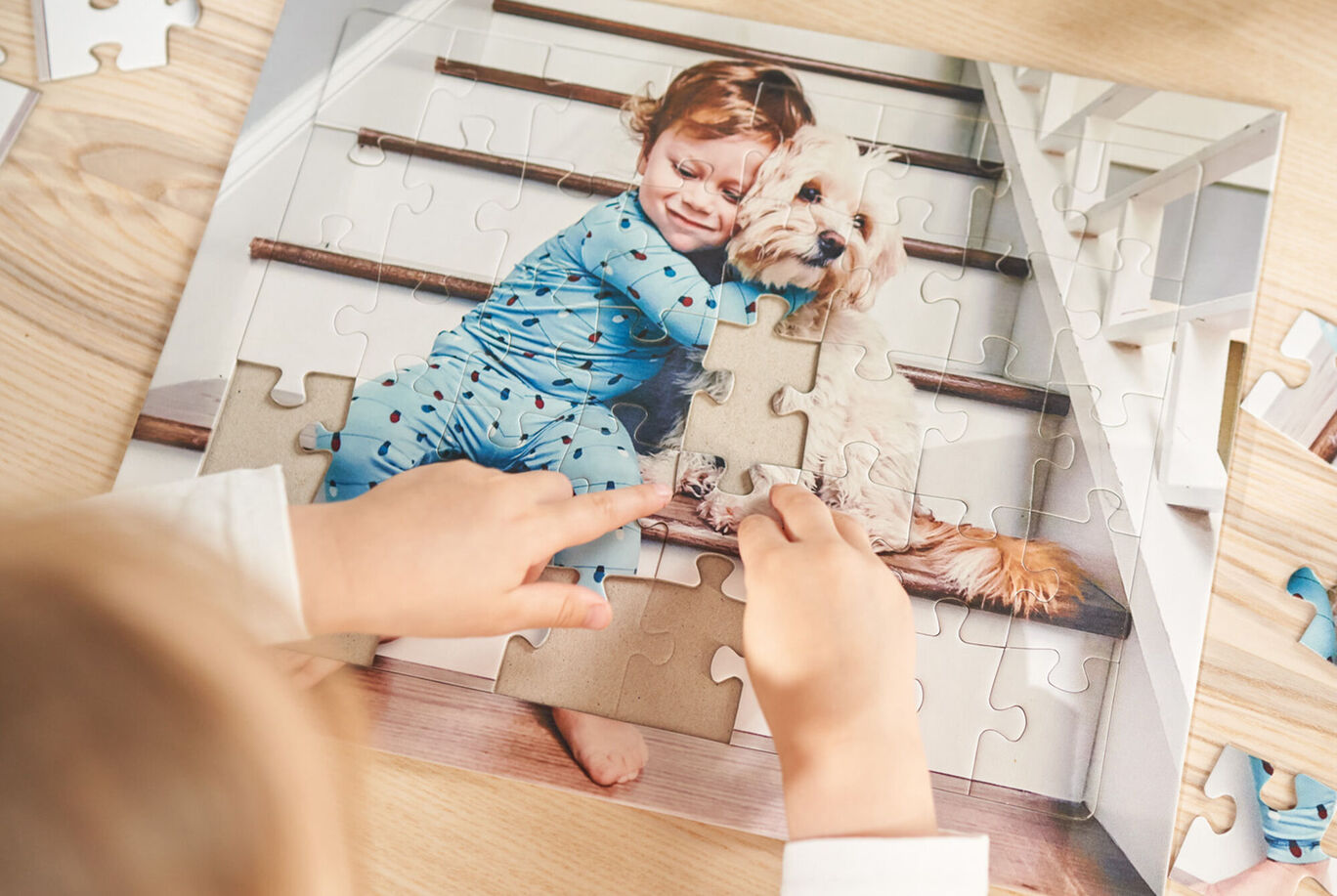 Un niño en pijama azul hace un rompecabezas con un perro en una escalera.
