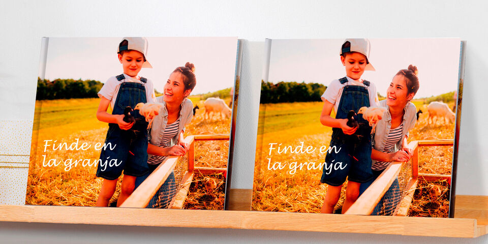 Un niño sostiene un pequeño animal en una granja, rodeado de un entorno rural. Muestra el CEWE FOTOBUCH "Finde en la granja".