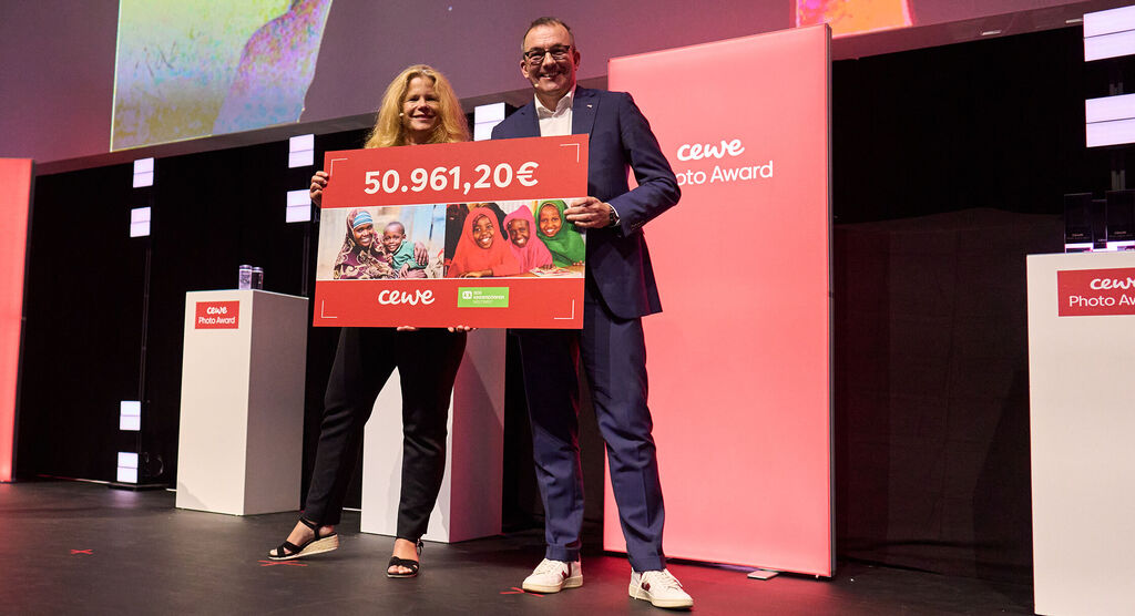 Dos personas sostienen un gran cartel de premio por 50.961,20 euros en el Premio CEWE Photo.