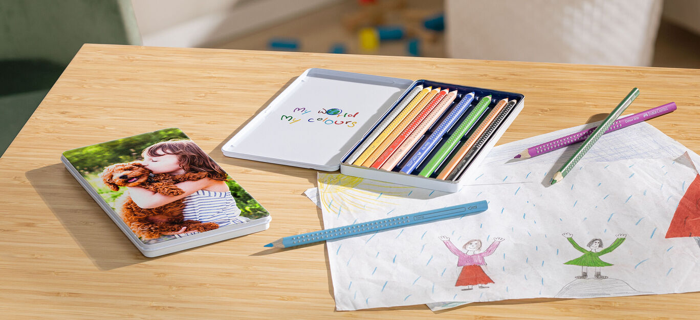 Una persona abraza a un perro, rodeada de lápices de colores y fotos sobre una mesa.