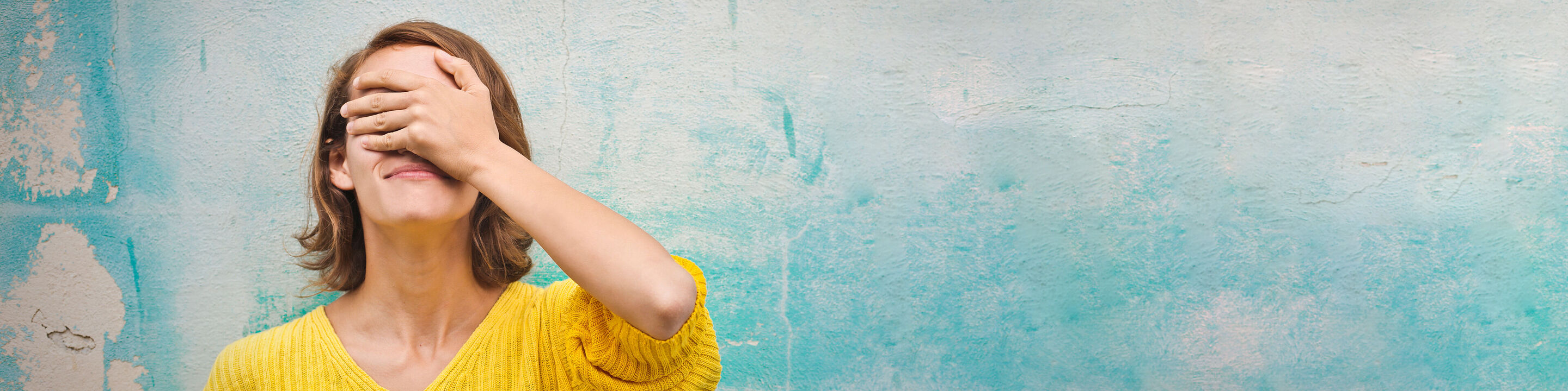 Una mujer con un suéter amarillo disfruta de un momento de tranquilidad ante una pared azul.