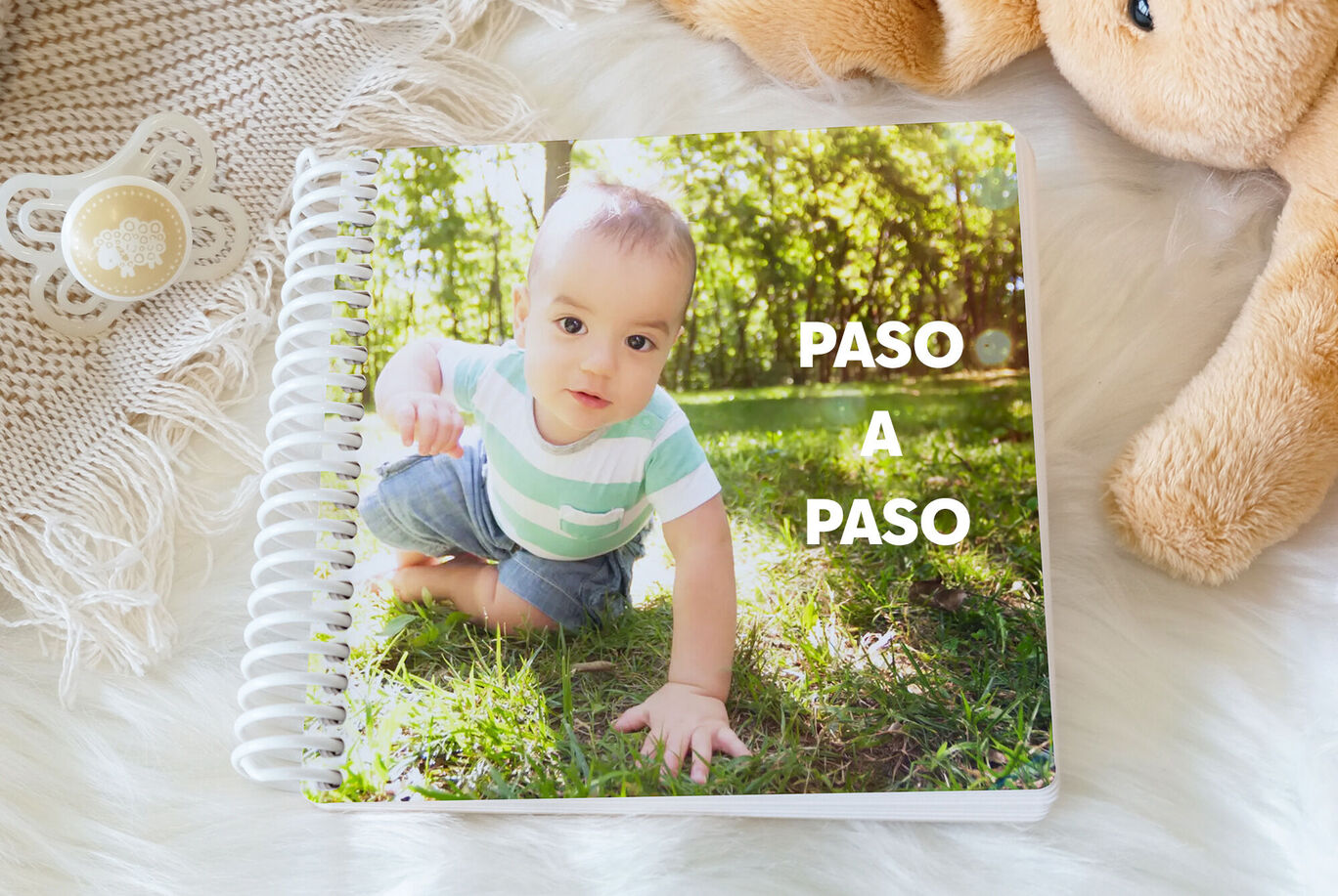 Un niño pequeño gatea alegremente sobre un césped verde. Junto a él hay un peluche y el título 'Paso a Paso'.