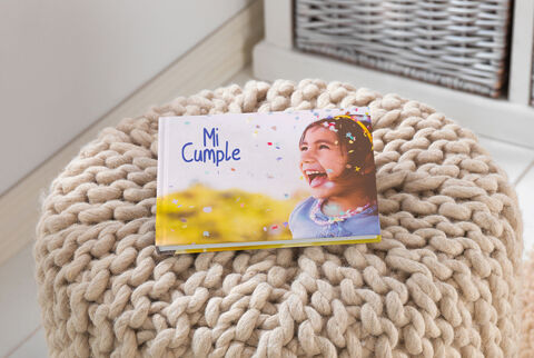 Un CEWE Photo Book titulado 'Mi Cumple' sobre un cómodo puf.