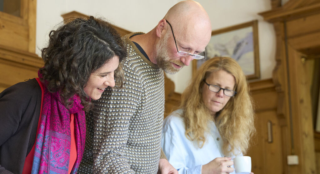 Tres personas en un ambiente acogedor ven algo juntos y muestran interés. Ambiente positivo presente.