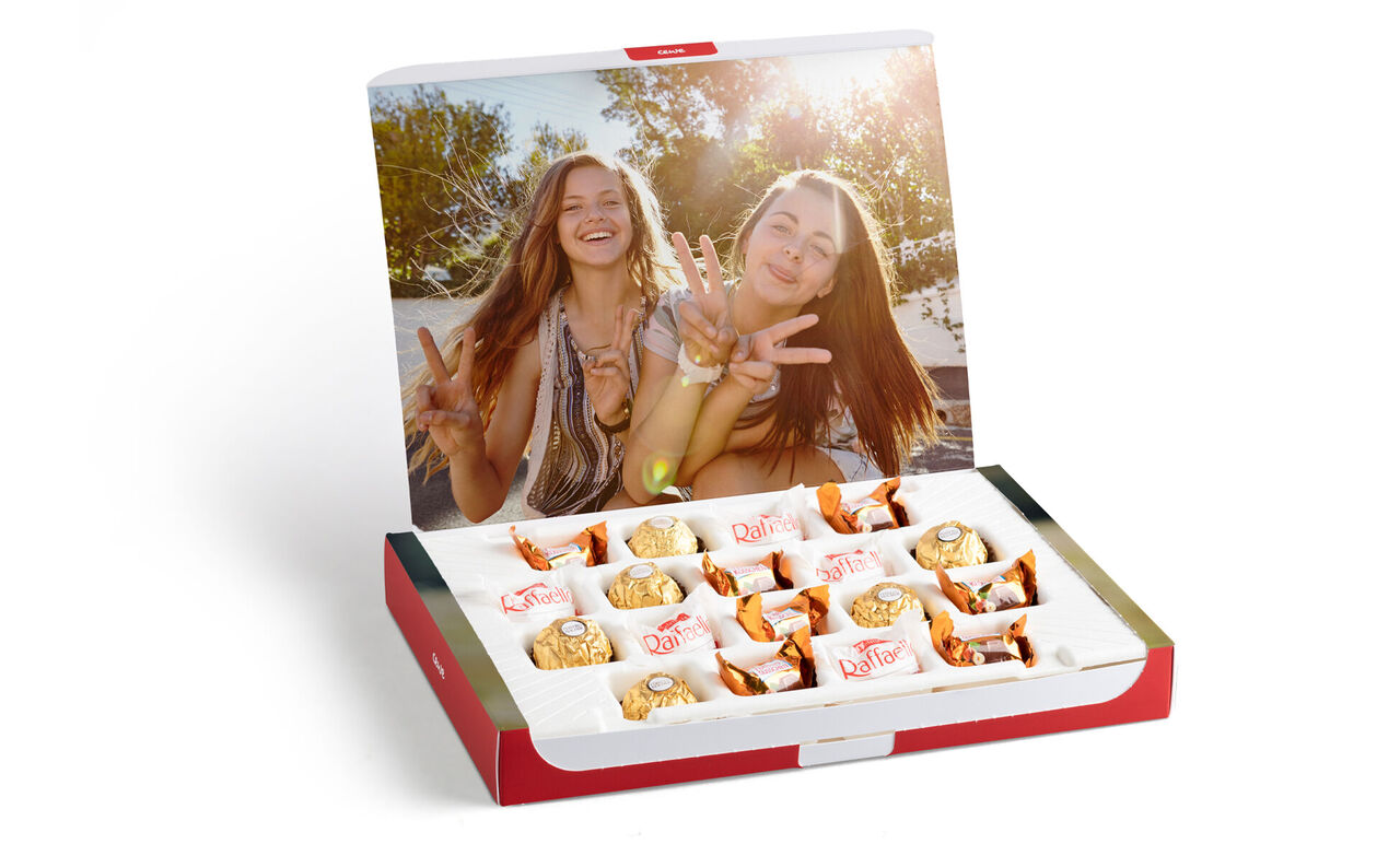 Dos amigas posan alegres frente a una caja de galletas, con el sol brillando y un ambiente relajado.