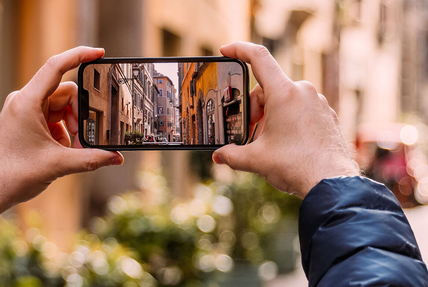 Manos sosteniendo un smartphone en horizontal fotografiando una calle con edificios de piedra.
