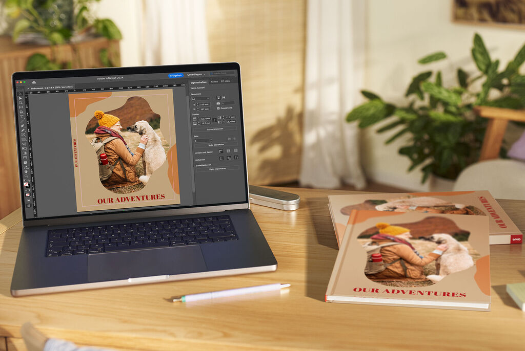 Un laptop muestra un diseño creativo con una foto de aventuras, al lado hay CEWE fotobooks.
