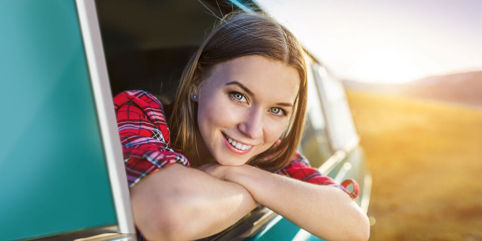La niña se asoma por la ventana de un coche y disfruta del sol de la tarde durante un viaje.