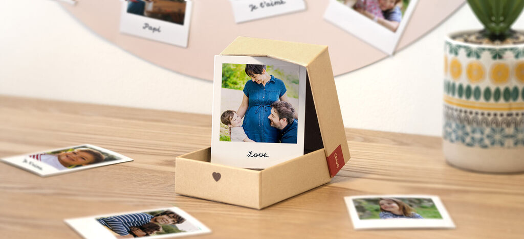 Una caja llena de fotos que muestran recuerdos personales de manera creativa. Enfocada en una imagen de una pareja feliz mirando a una mujer embarazada.