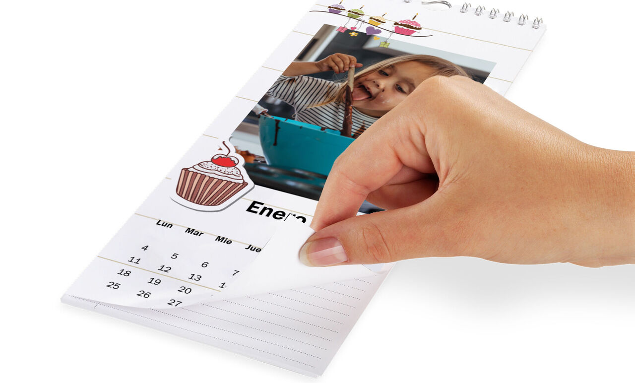 Una mano hojeando un calendario mientras un niño sostiene una taza de chocolate.