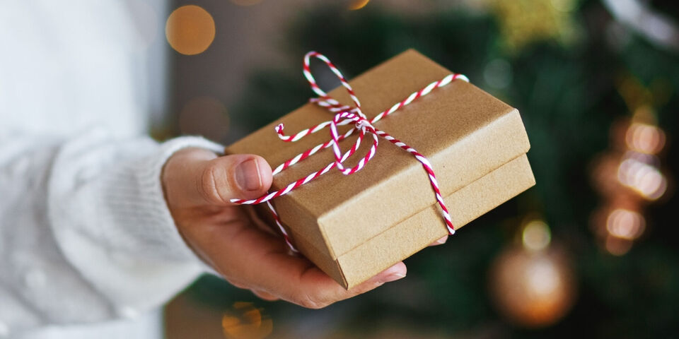 Una persona sostiene un regalo cuidadosamente envuelto con cinta roja y blanca.