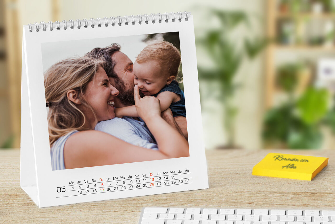 Un calendario sobre una mesa muestra una escena familiar con un adulto y un niño, fondo borroso con plantas verdes.
