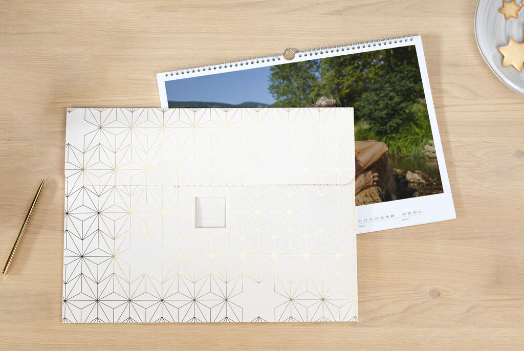 Un hermoso calendario CEWE sobre una superficie de madera, junto a una elegante funda A4.