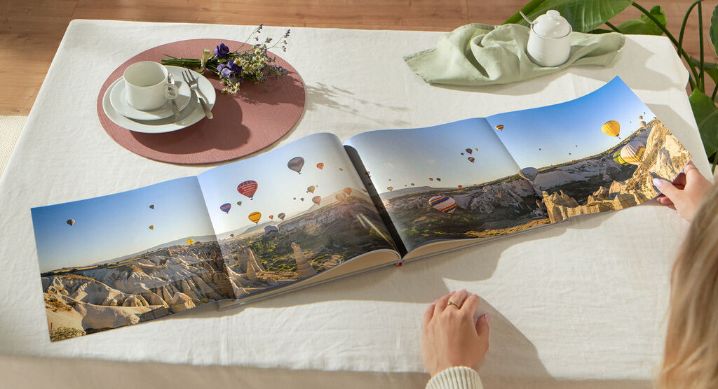 Una persona hojea un fotolibro abierto con globos y paisajes al fondo