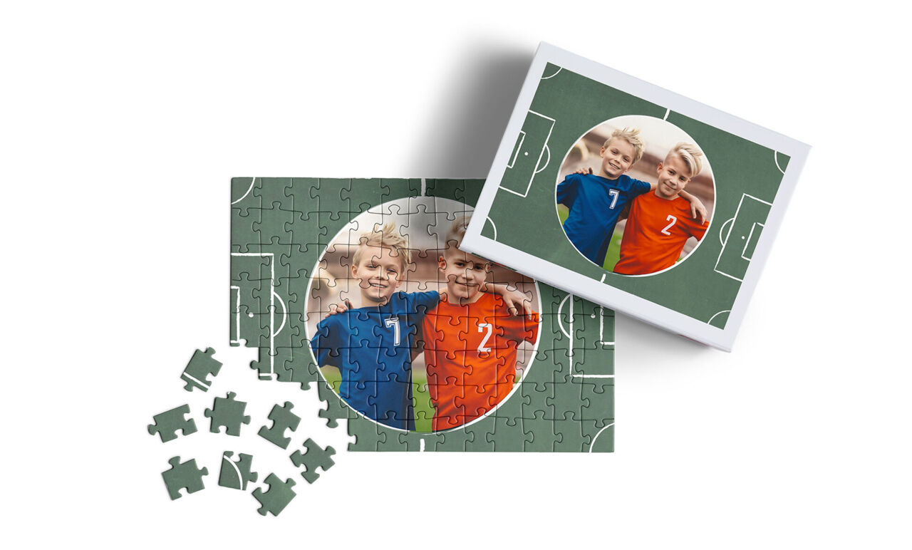 Un puzzle personalizado de un campo de fútbol verde con una foto circular de dos niños abrazados. El puzzle está incompleto con piezas
