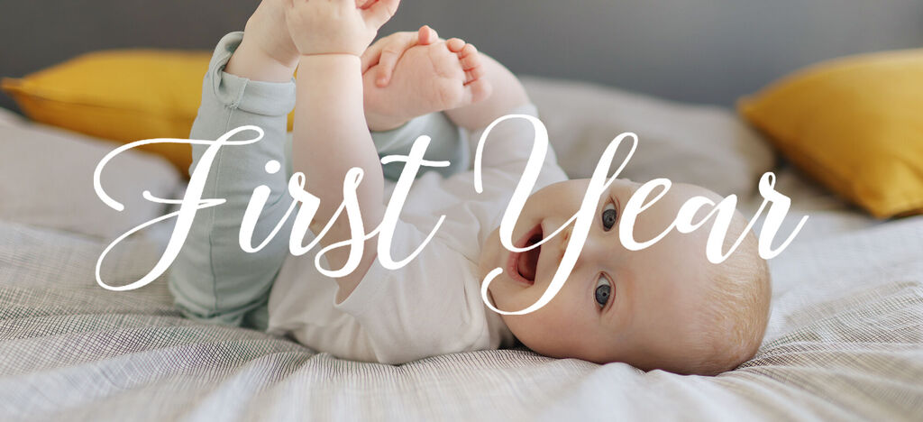 Un bebé juega en una cama, levantando las piernas, rodeado de cojines.